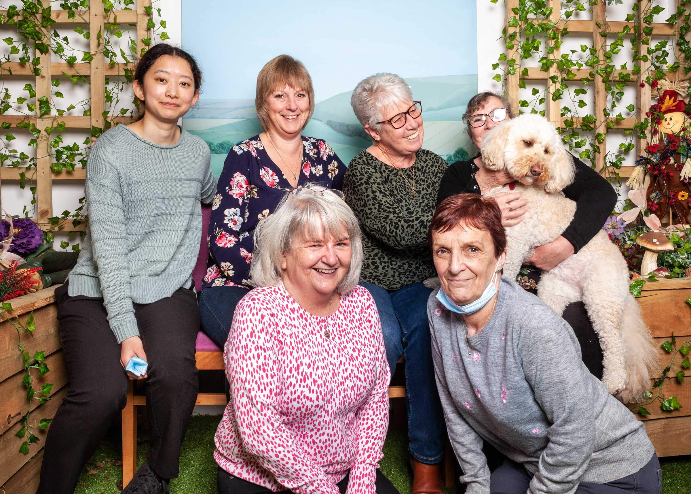A lovely group picture of six ladies and one dog, being lifted up, all smiling for the picture, sitting in Old Silk Works Club