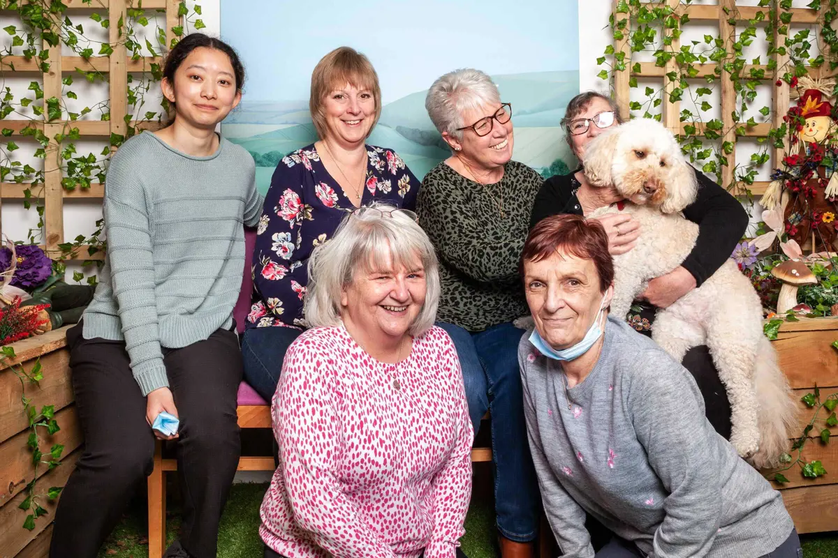 A lovely group picture of six ladies and one dog, being lifted up, all smiling for the picture, sitting in Old Silk Works Club