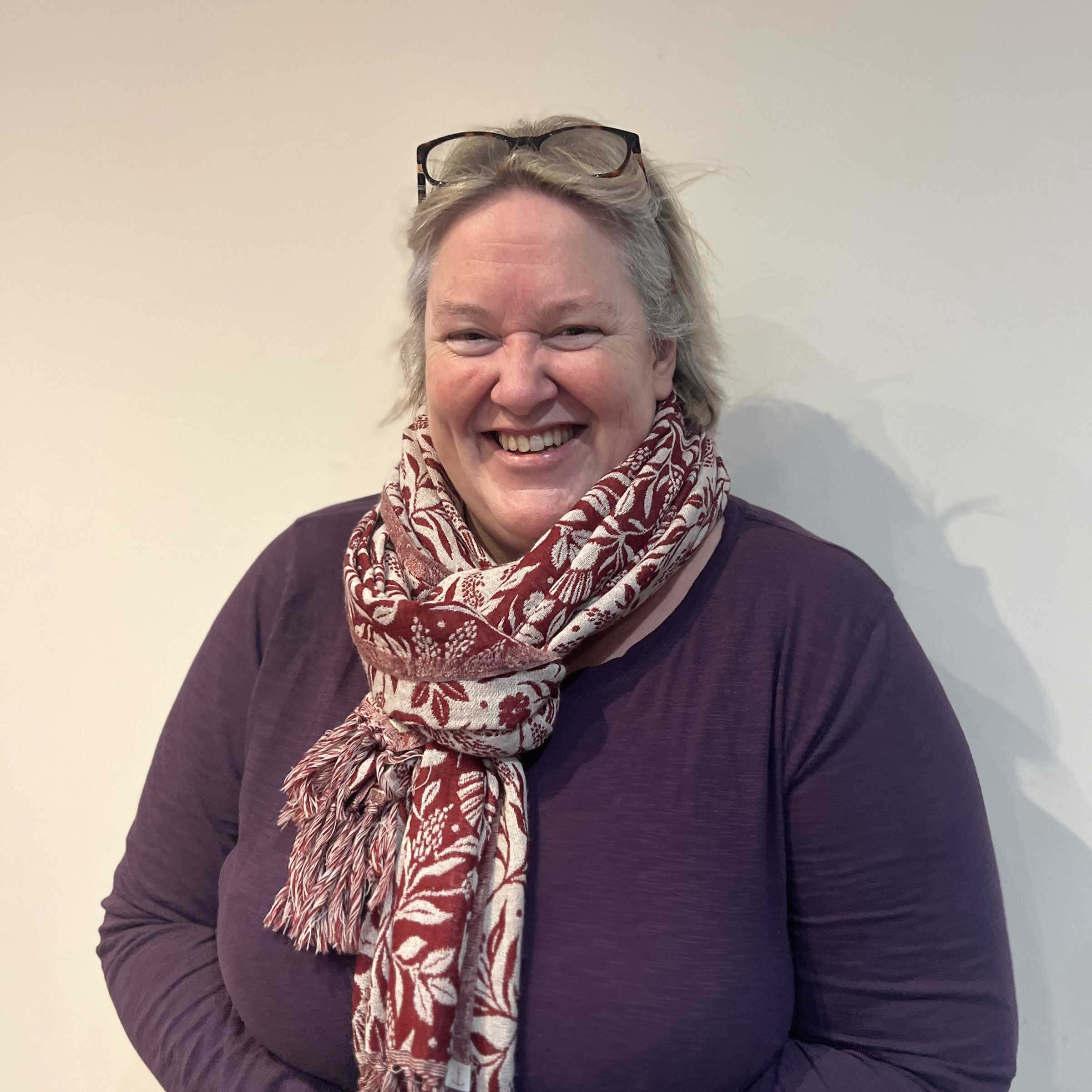 headshot of Stacey smiling broadly, wearing a purple top and patterned scarf