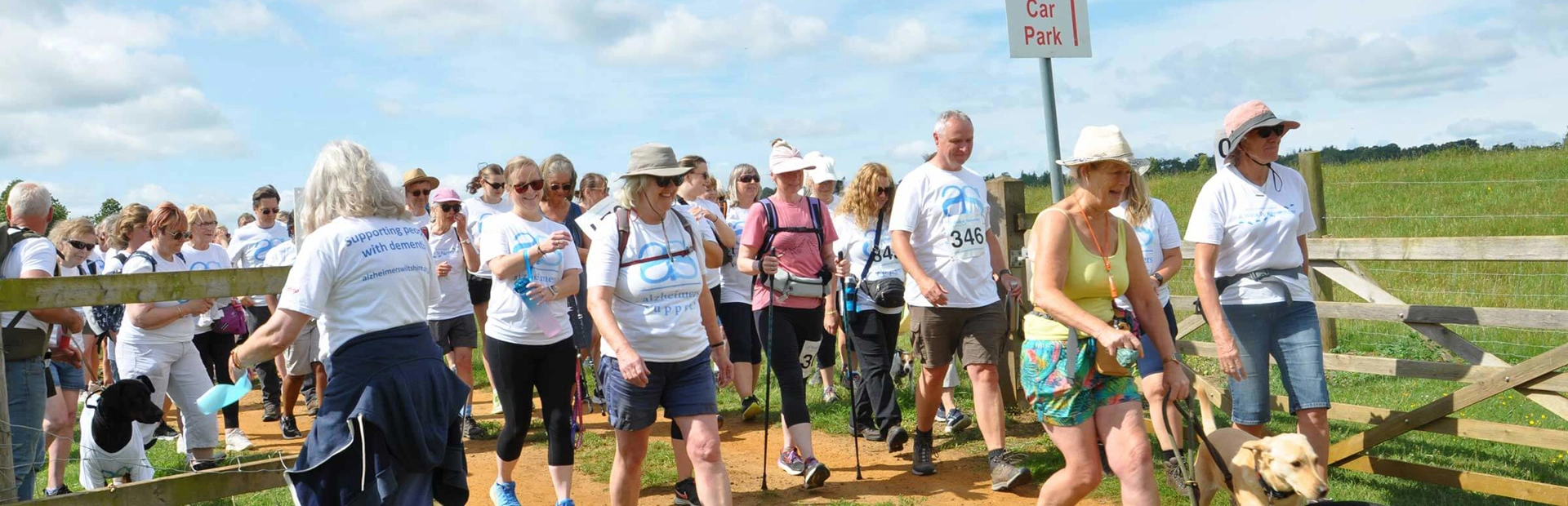 A crowd of walkers starting out together through a wide gate. It's a blue-sky day and most are wearing shorts and charity branded white T-shirts A crowd of walkers starting out together through a wide gate. It's a blue-sky day and most are wearing shorts and charity branded white T-shirts