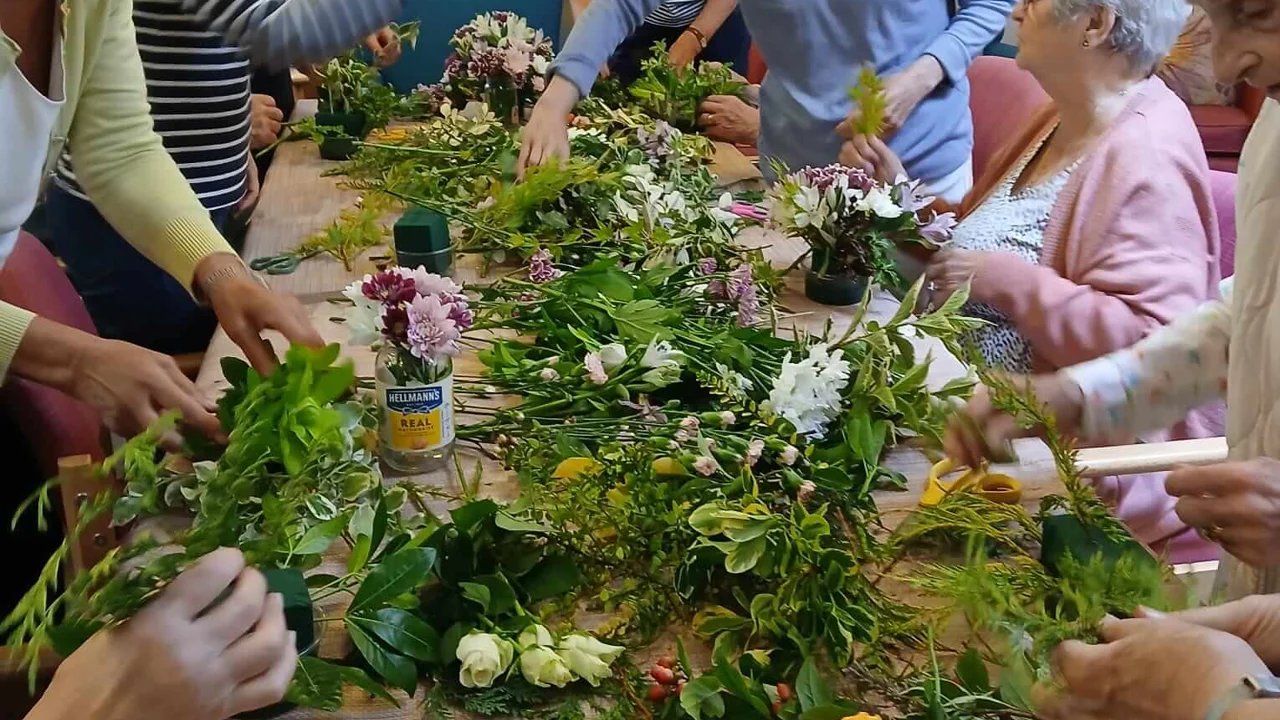 Group of women in Sidmouth Street Club choosing flowers from a table covered in greenery and pink, white and yellow flowers