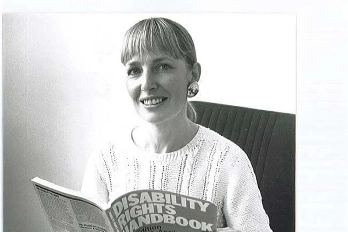 A young Anna Littlechild seated at a desk looking at a disability rights handbook, black and white