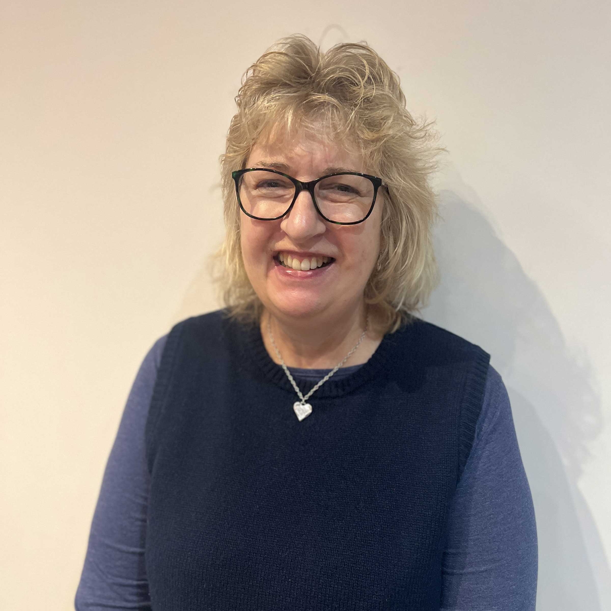 Hilary smiling at the camera wearing a blue knitted tanktop and glasses