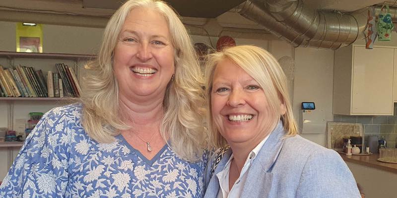 Two CEOs Sarah Marriott and Babs Harris, standing very close together, both wearing light blue, smiling