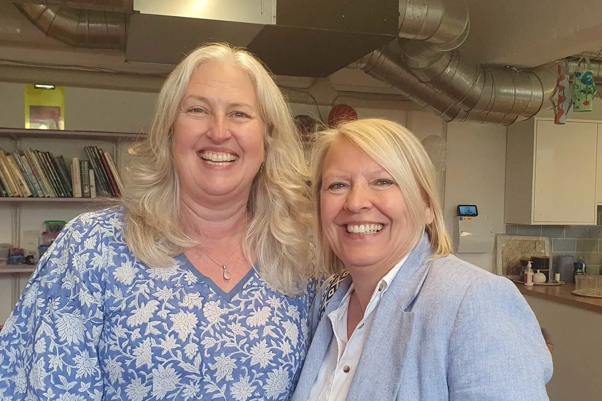 Two CEOs Sarah Marriott and Babs Harris, standing very close together, both wearing light blue, smiling