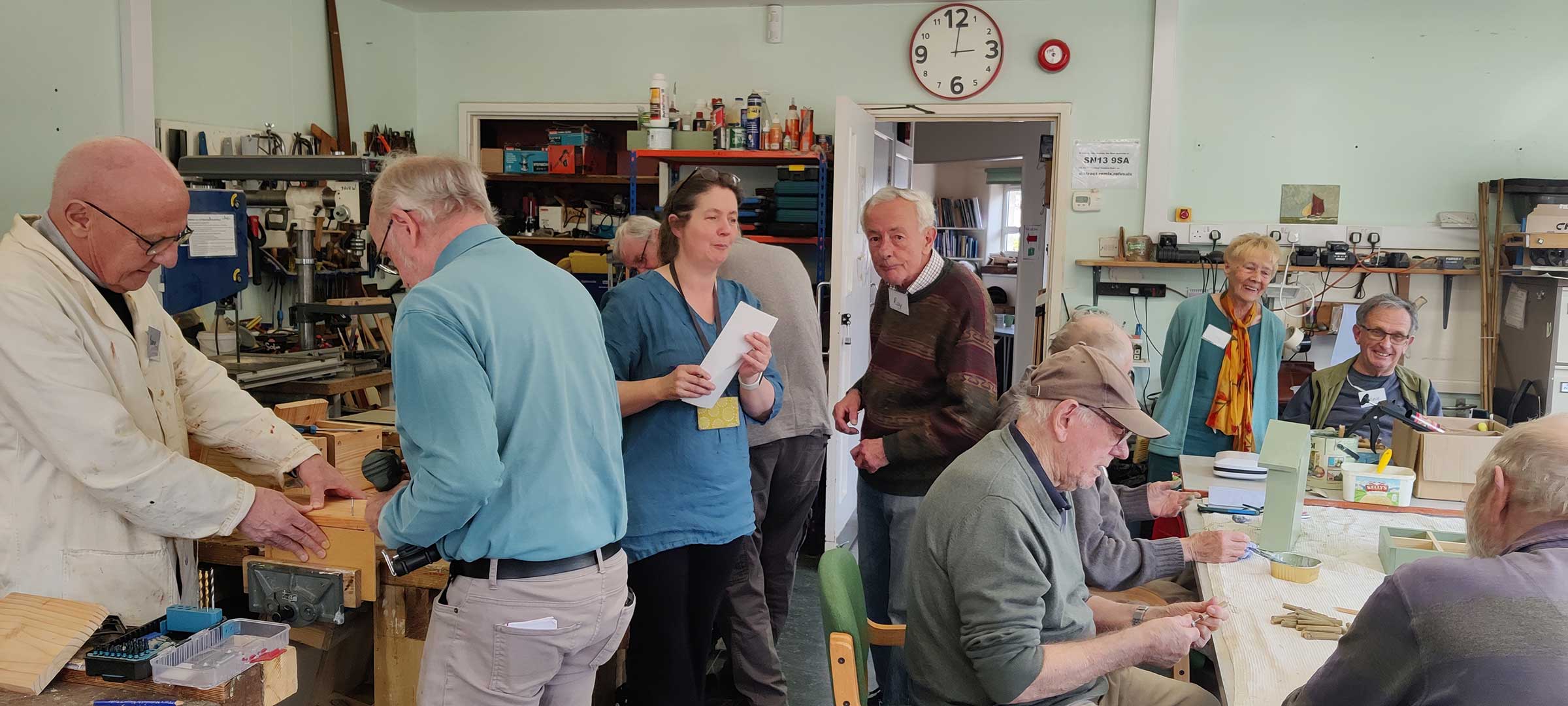 Groups of mostly older men taking part in practical woodworking activities and using tools inside the memory shed building