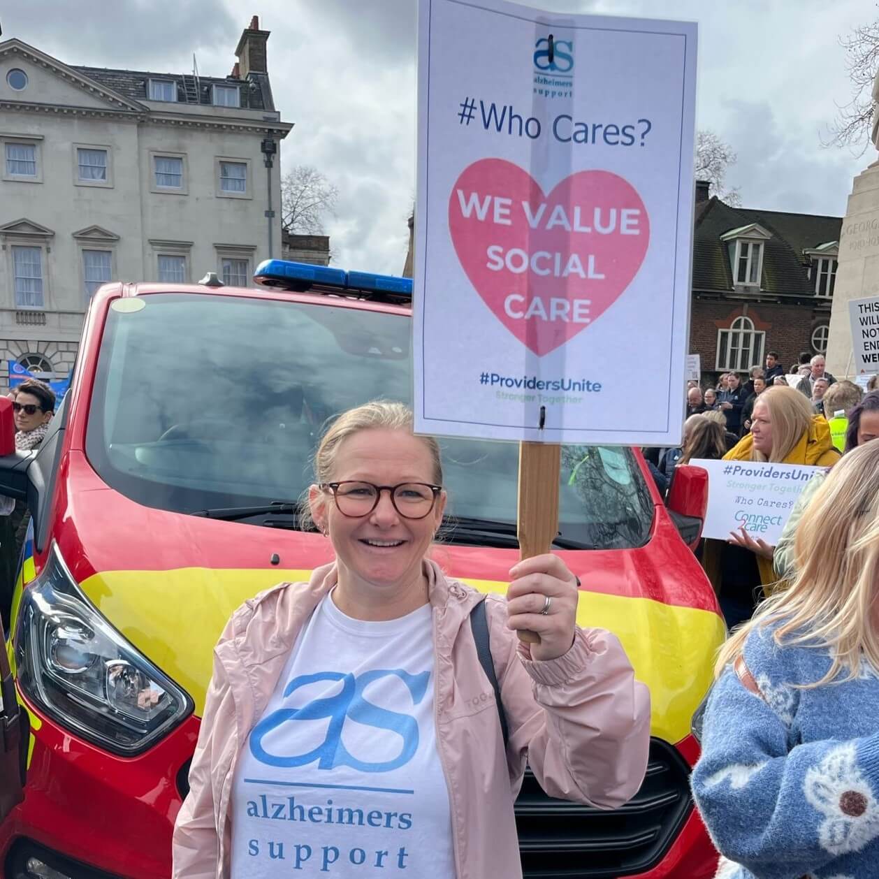 Monique on the march in front of a support vehicle, smiling and holding a We Value Social Care banner