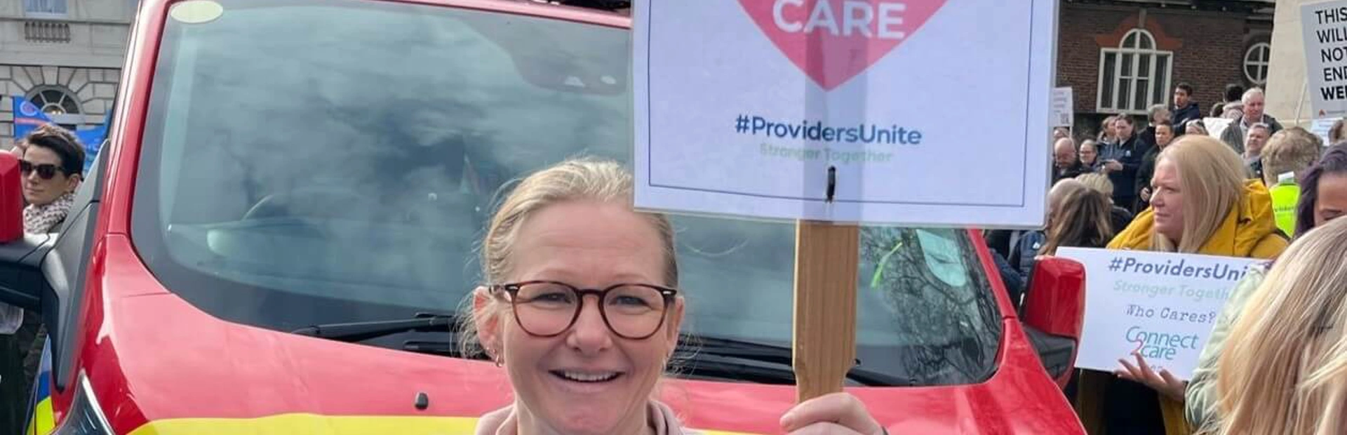Monique on the march in front of a support vehicle, smiling and holding a We Value Social Care banner Monique on the march in front of a support vehicle, smiling and holding a We Value Social Care banner