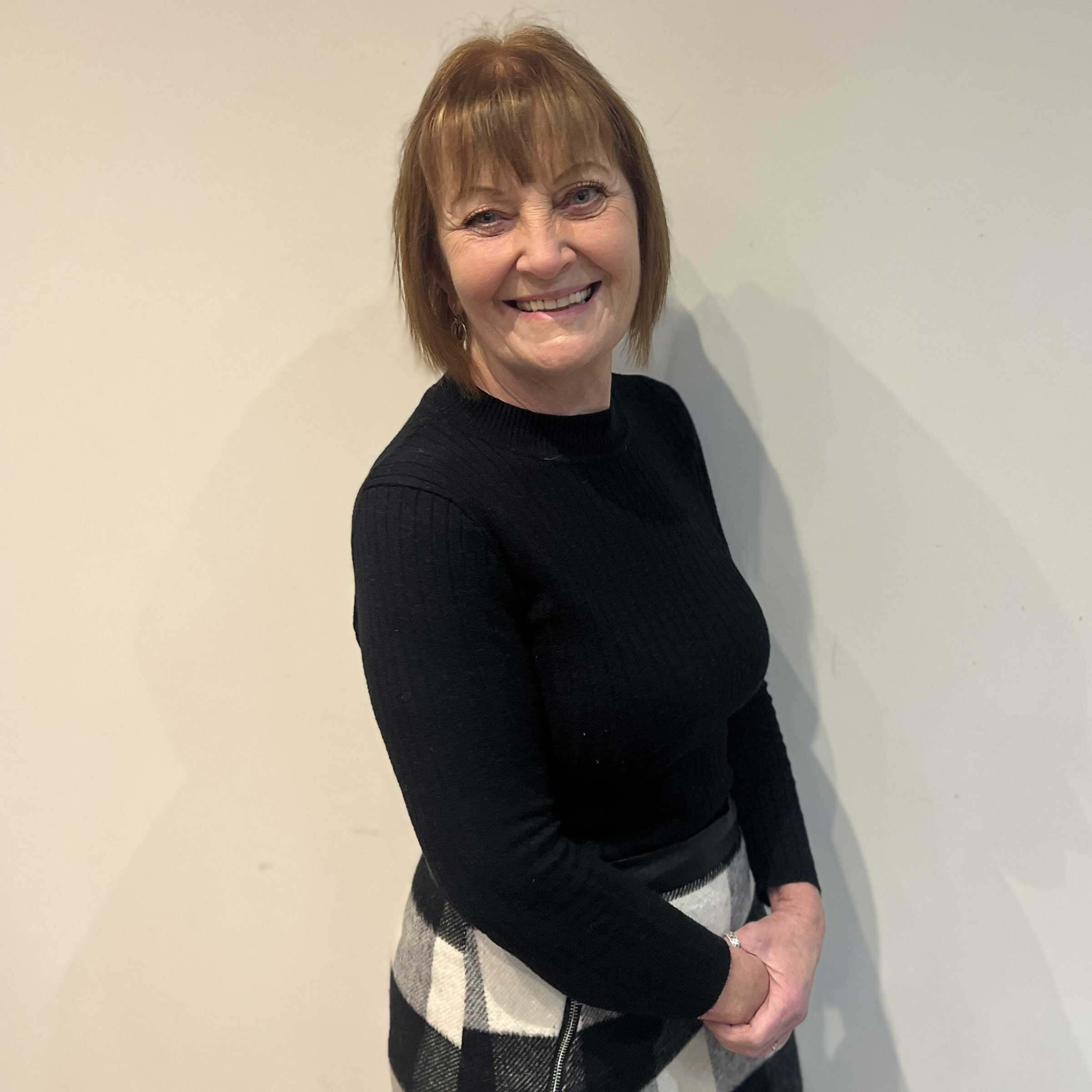 Headshot of Sharon turning to smile at the camera, in a black top