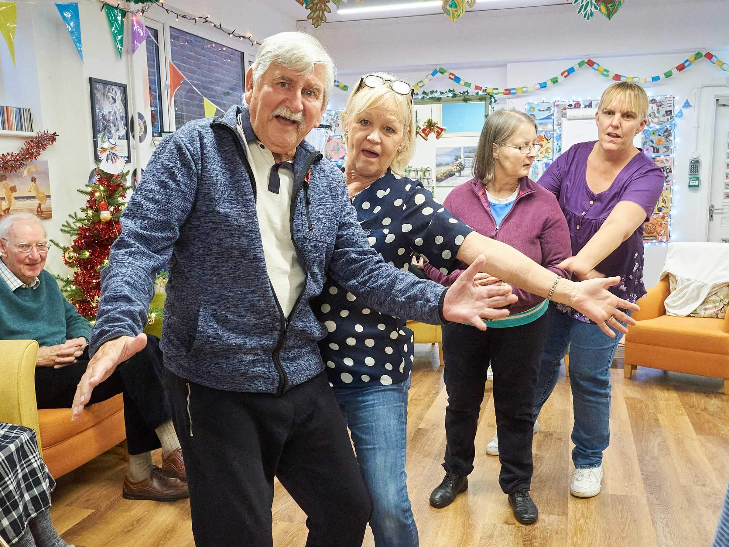 A man and three ladies dancing and waving in Mill Street Club with Christmas decorations 