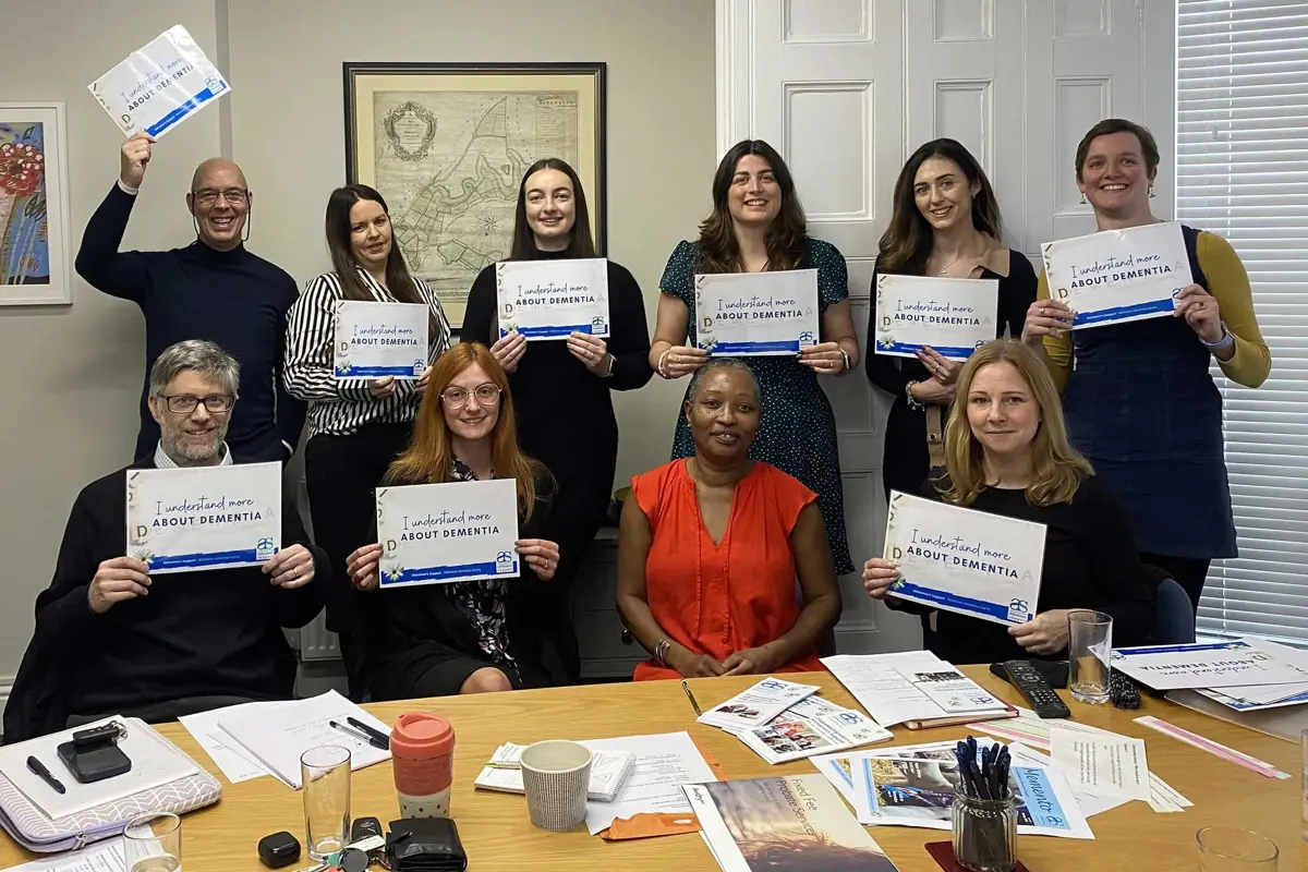 A group of ten people, some standing, some sitting, all holding their I understand more about Dementia certificates with Annie Clayton sat in a red top in the middle