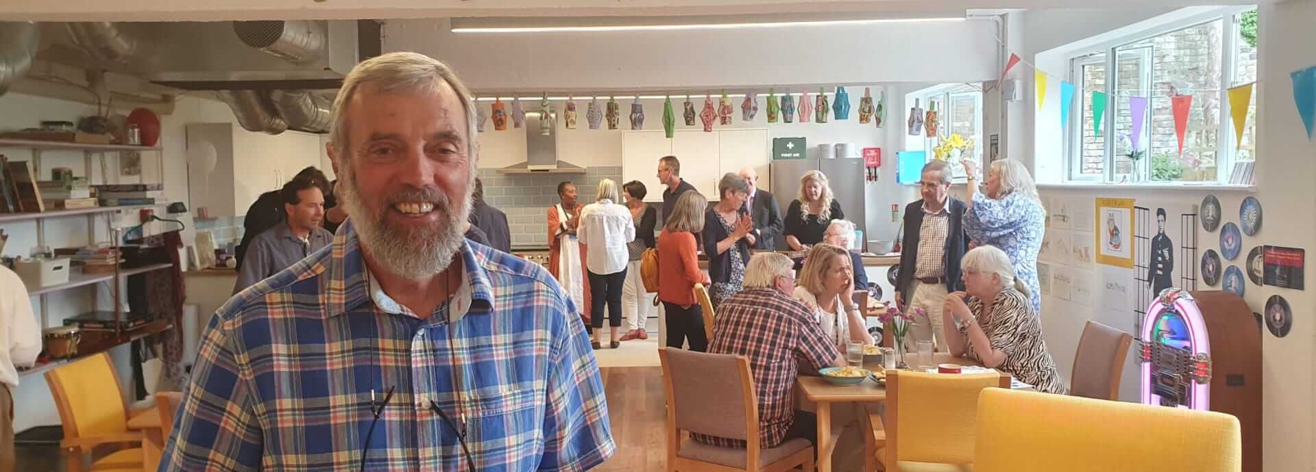 A bearded man with a checked shirt looking at us with a group of people chatting at a party behind him at Scots Lane Club