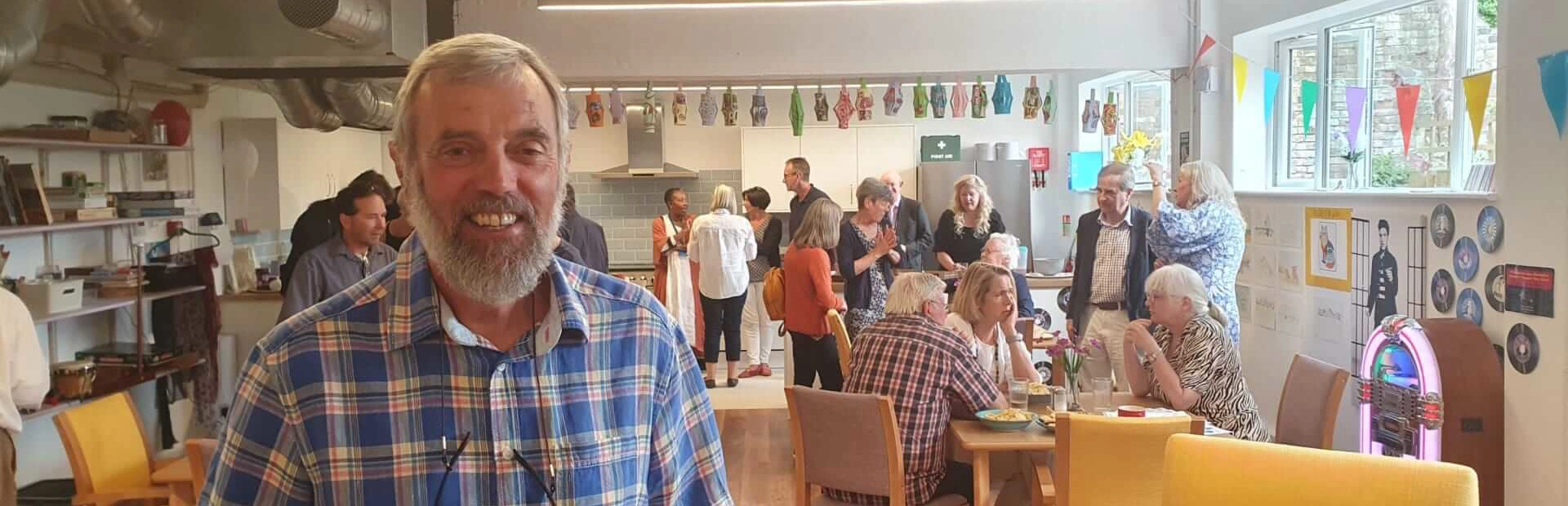 A bearded man with a checked shirt looking at us with a group of people chatting at a party behind him at Scots Lane Club A bearded man with a checked shirt looking at us with a group of people chatting at a party behind him at Scots Lane Club