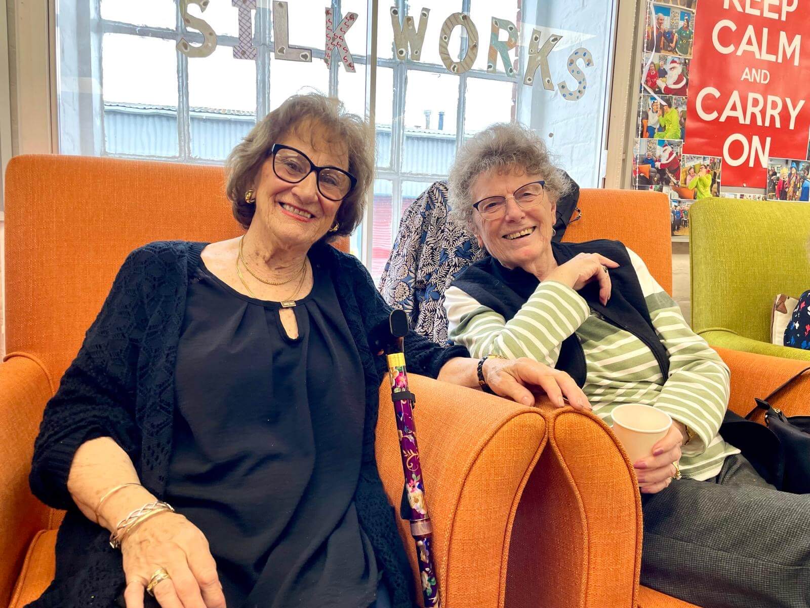Two older female club members sitting together in orange armchairs, smiling