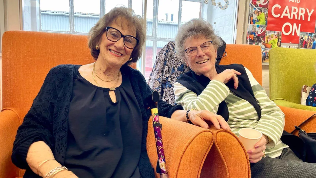 Two older female club members sitting together in orange armchairs, smiling