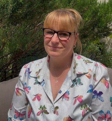 head and shoulders of Kelly, with her hair up and wearing brown glasses and a top printed with butterflies