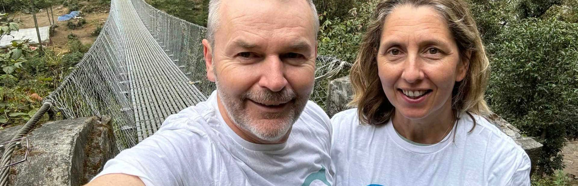 A close up selfie taken by Kate and Nigel with a thin rope and wire bridge behind them whilst doing an Everest Base Camp walk A close up selfie taken by Kate and Nigel with a thin rope and wire bridge behind them whilst doing an Everest Base Camp walk
