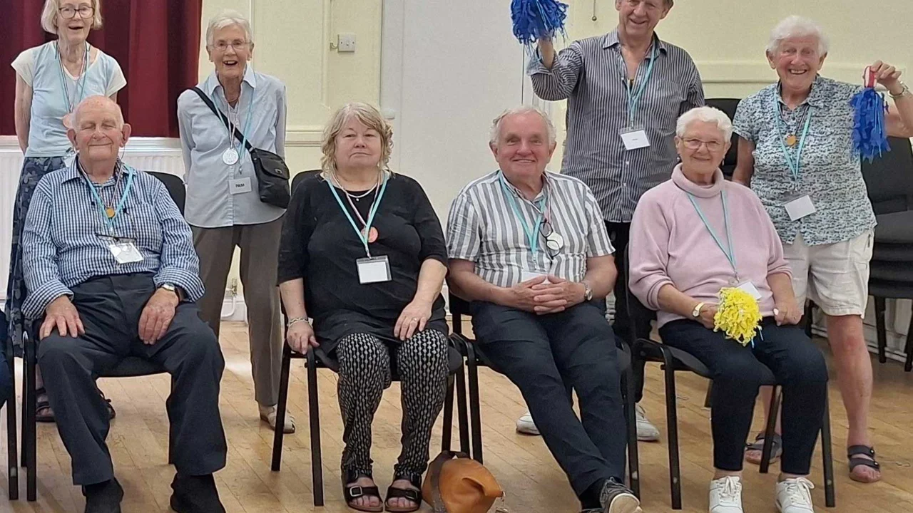 Four people sitting on chairs and four people standing behind them some waving blue and yellow pom poms at Amesbury Movement for the Mind