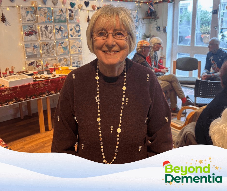Pam in a brown sparkly jumper and chunky necklace, smiling at the camera with Mill St club members in the background.