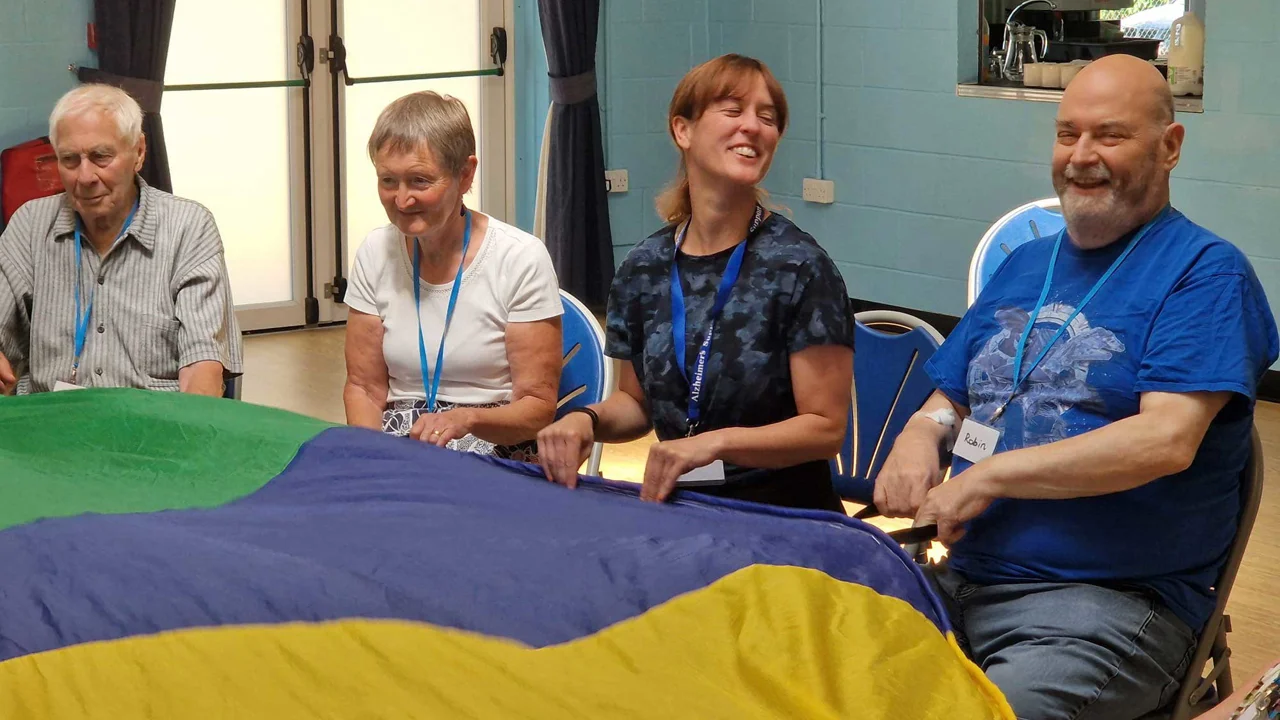 Four people holding a blue, yellow and green parachute in front of them, all smiling at Melksham Movement for the Mind