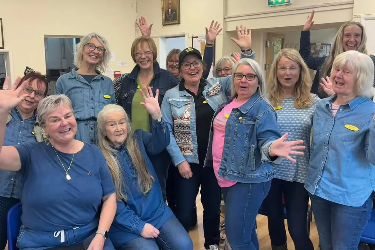 A group of ladies all wearing Denim for Dementia blue, standing, sitting, waving and smiling at the camera