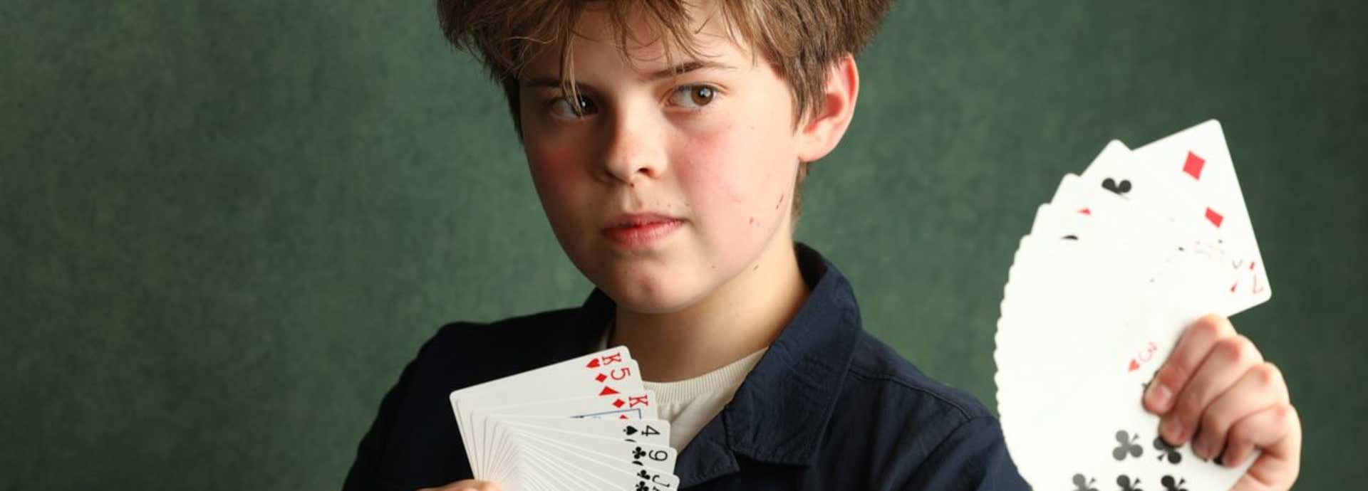 Close up professional picture of Oli, our magician, holding up cards in fan shape in both hands looking outwards 
