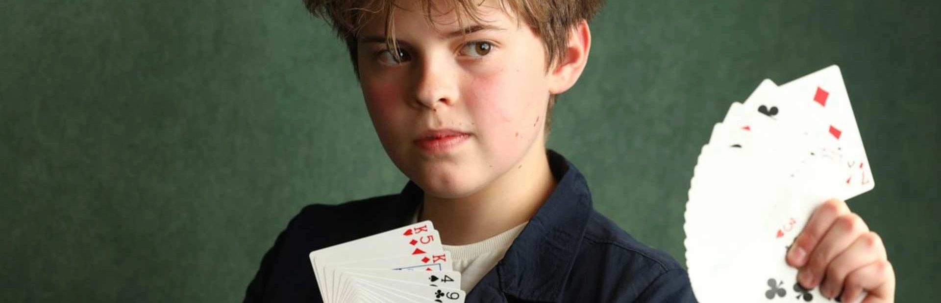 Close up professional picture of Oli, our magician, holding up cards in fan shape in both hands looking outwards Close up professional picture of Oli, our magician, holding up cards in fan shape in both hands looking outwards