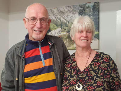 A man in a stripy coloured rugby top with a lady in a patterned top, facing the camera and both are smiling