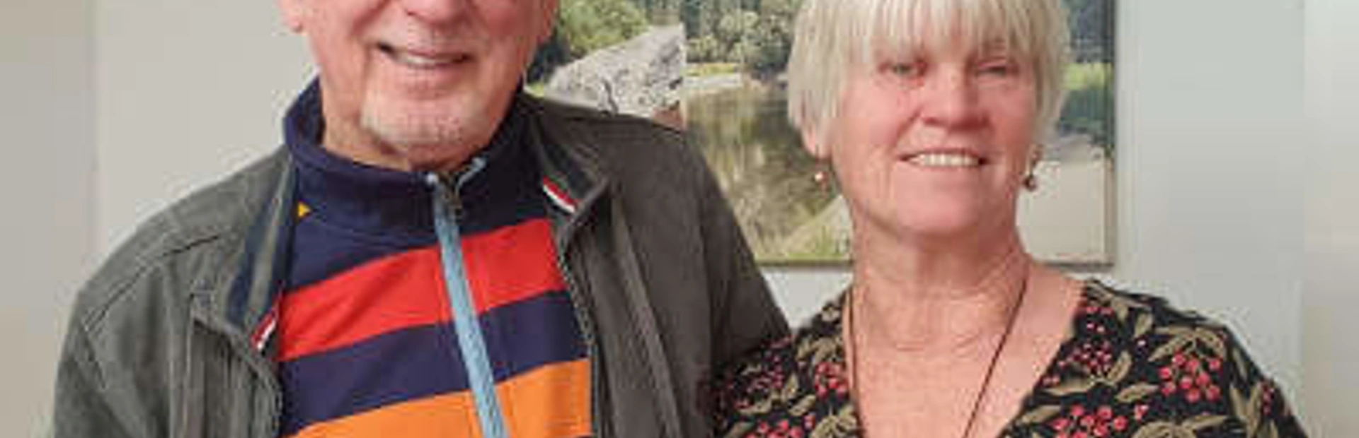 A man in a stripy coloured rugby top with a lady in a patterned top, facing the camera and both are smiling A man in a stripy coloured rugby top with a lady in a patterned top, facing the camera and both are smiling