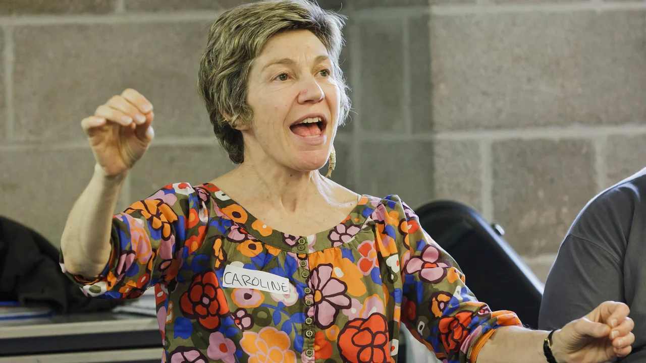 Close up of music teacher Caroline in full voice conducting the group with her hands.