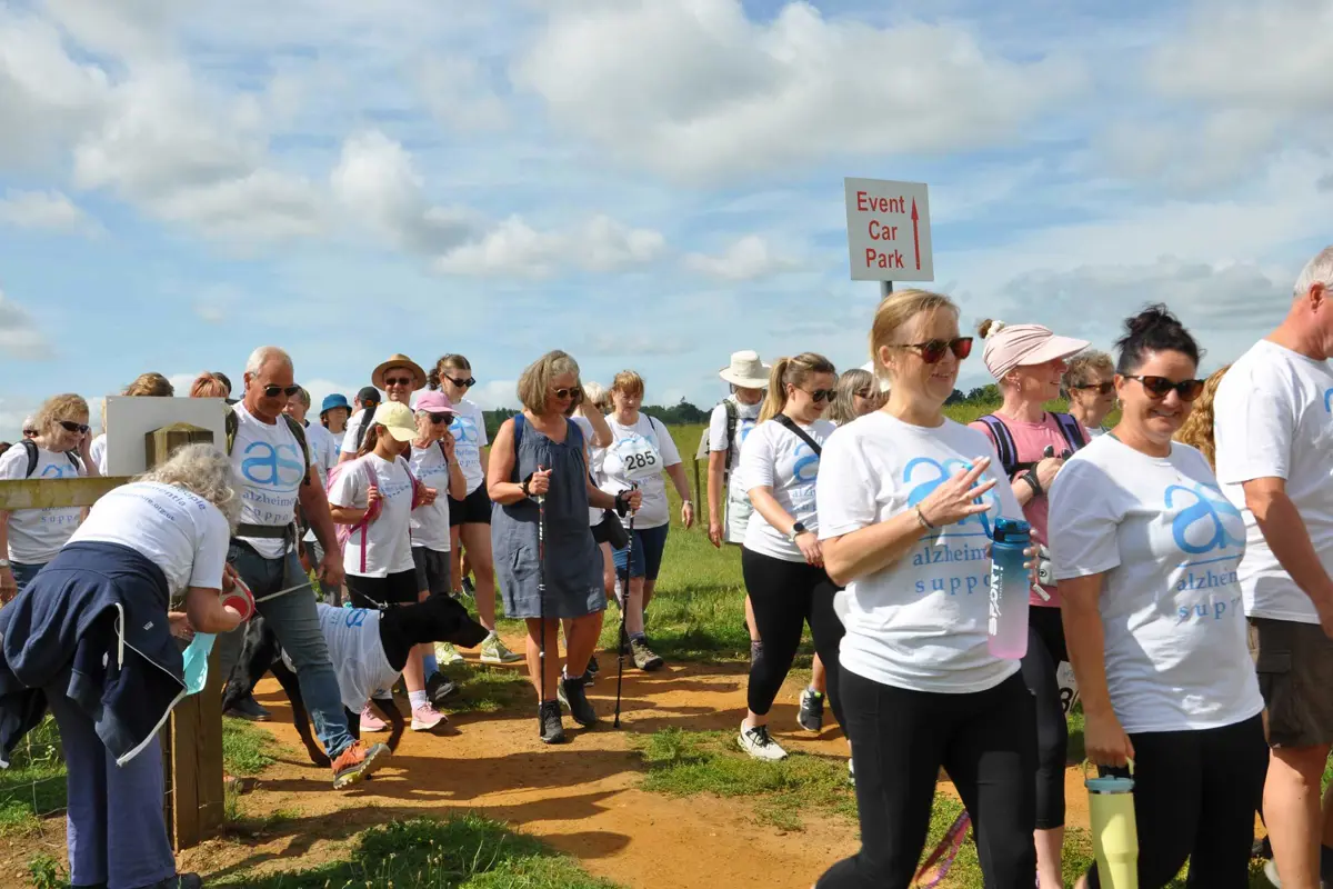 A group of men and women just after the ribbon cutting to start the Bowood Walk to Remember. Some are looking at the camera, some looking ahead, some walking with a dog, some with sticks, some with hats and sunglasses.