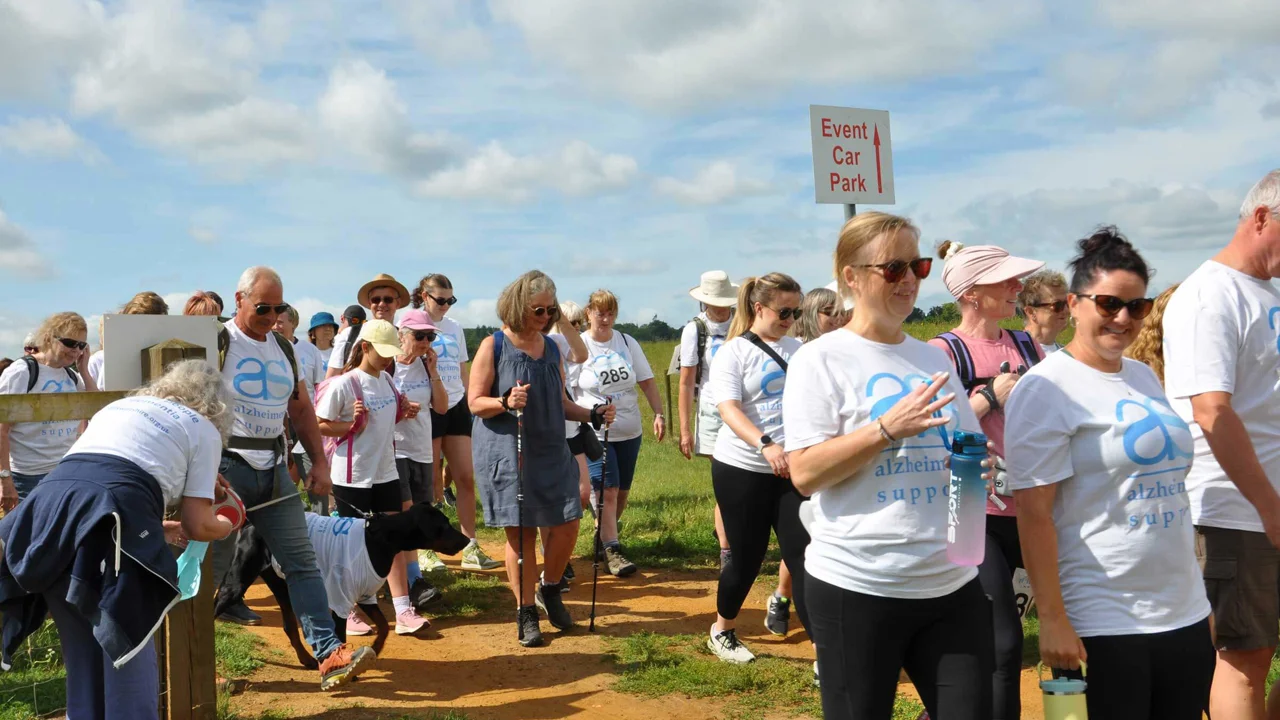 A group of men and women just after the ribbon cutting to start the Bowood Walk to Remember. Some are looking at the camera, some looking ahead, some walking with a dog, some with sticks, some with hats and sunglasses.