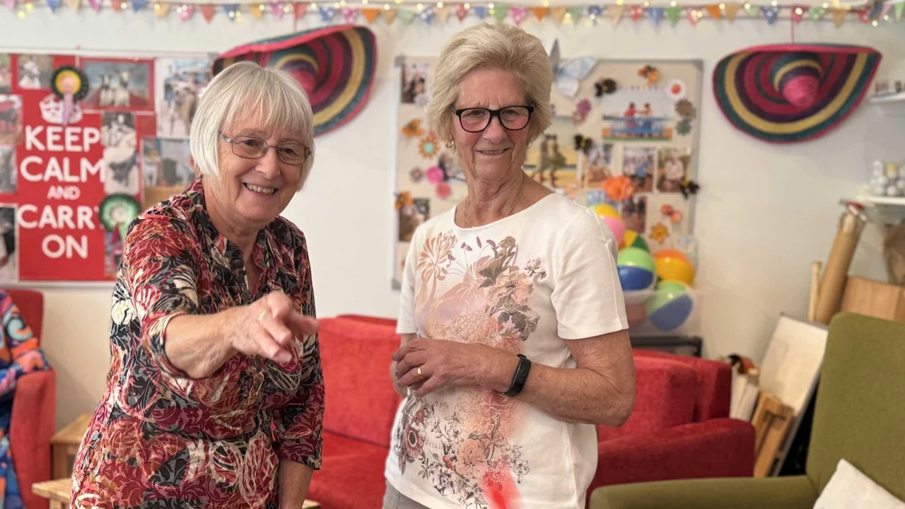 A lady wearing pink top throwing a dart with a lady next to her smiling and watching at Mill Street Club