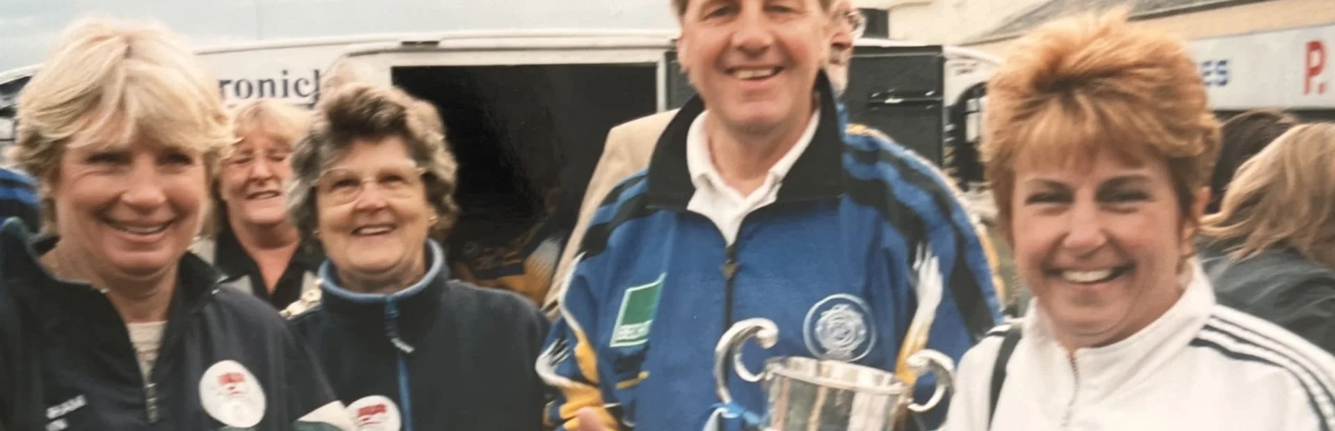 A lady in a white tracksuit holding a gold football cup with a gentleman and two ladies smiling beside her A lady in a white tracksuit holding a gold football cup with a gentleman and two ladies smiling beside her