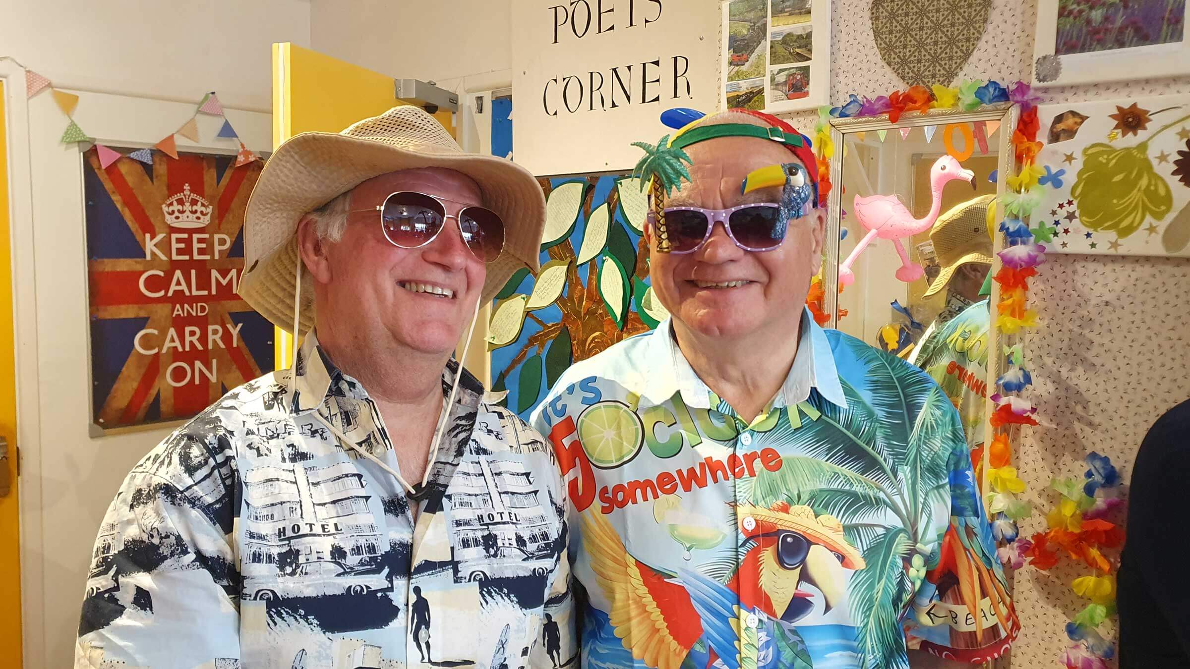 Two gentlemen volunteers wearing hats, sunglasses and Hawaiian shirts standing in Mill Street Club for a party 