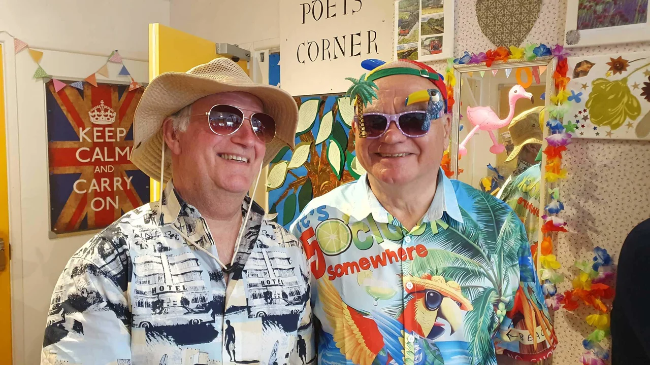 Two gentlemen volunteers wearing hats, sunglasses and Hawaiian shirts standing in Mill Street Club for a party