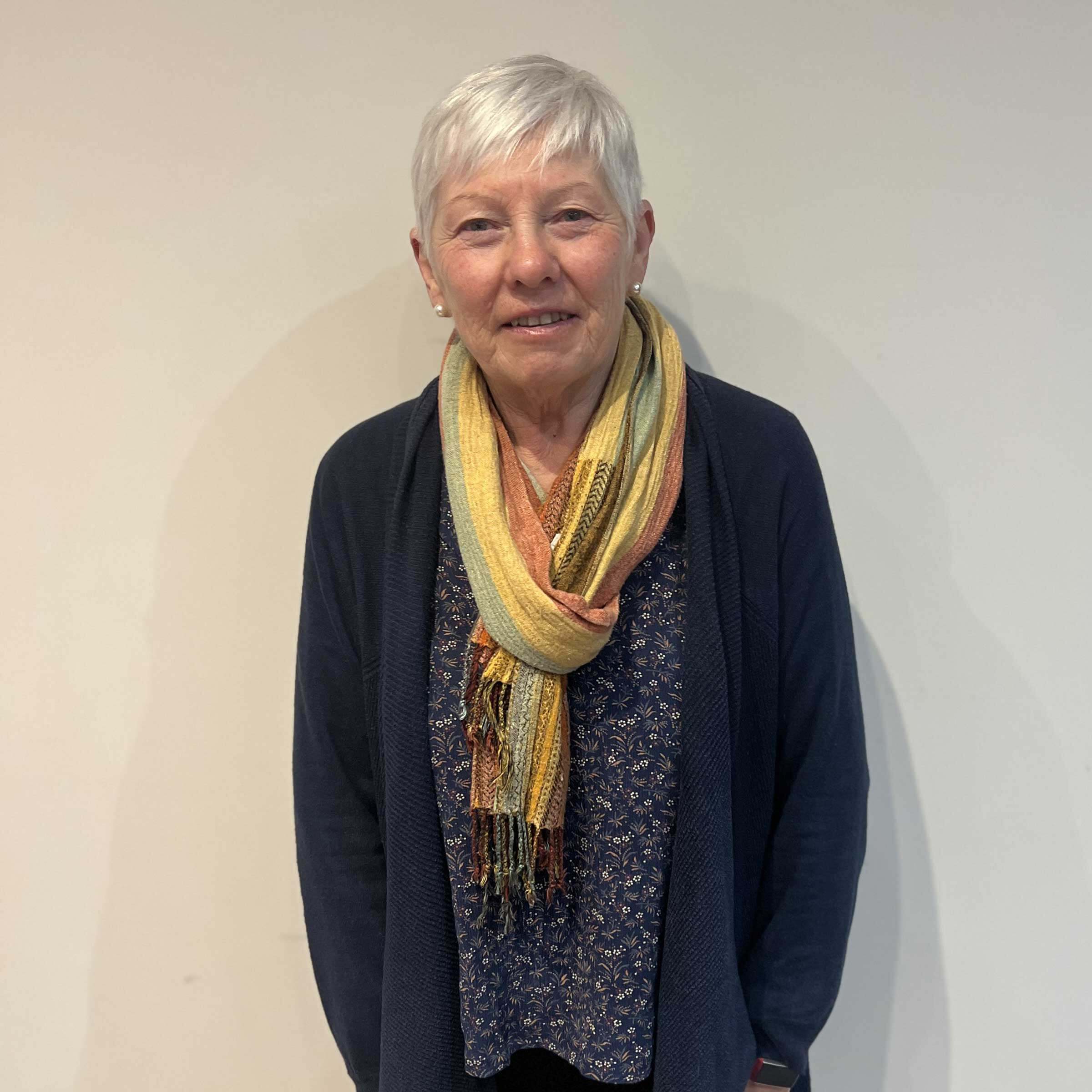 head and shoulders of Tina with short grey hair and wearing a blue cardigan and yellowy scarf