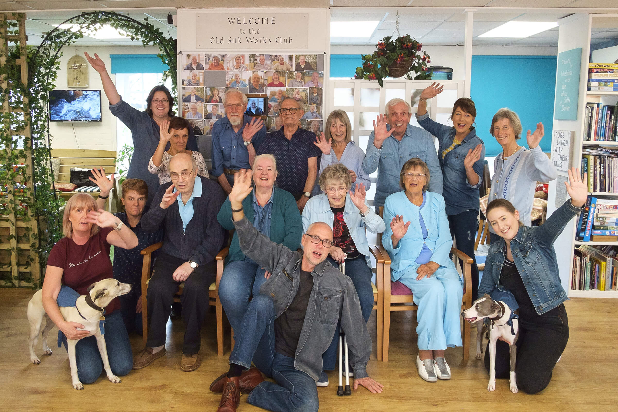 Group of club members staff and volunteers, some seated, some standing, wearing their demin outfits and waving for the camera
