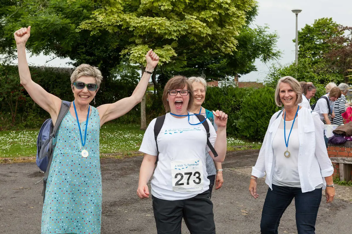 Four ladies cheering and smiling with Walk to Remember medals on standing in a park with a tree behind them