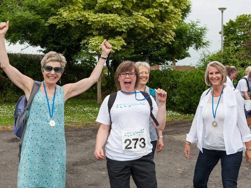 Four ladies cheering and smiling with Walk to Remember medals on standing in a park with a tree behind them  Four ladies cheering and smiling with Walk to Remember medals on standing in a park with a tree behind them
