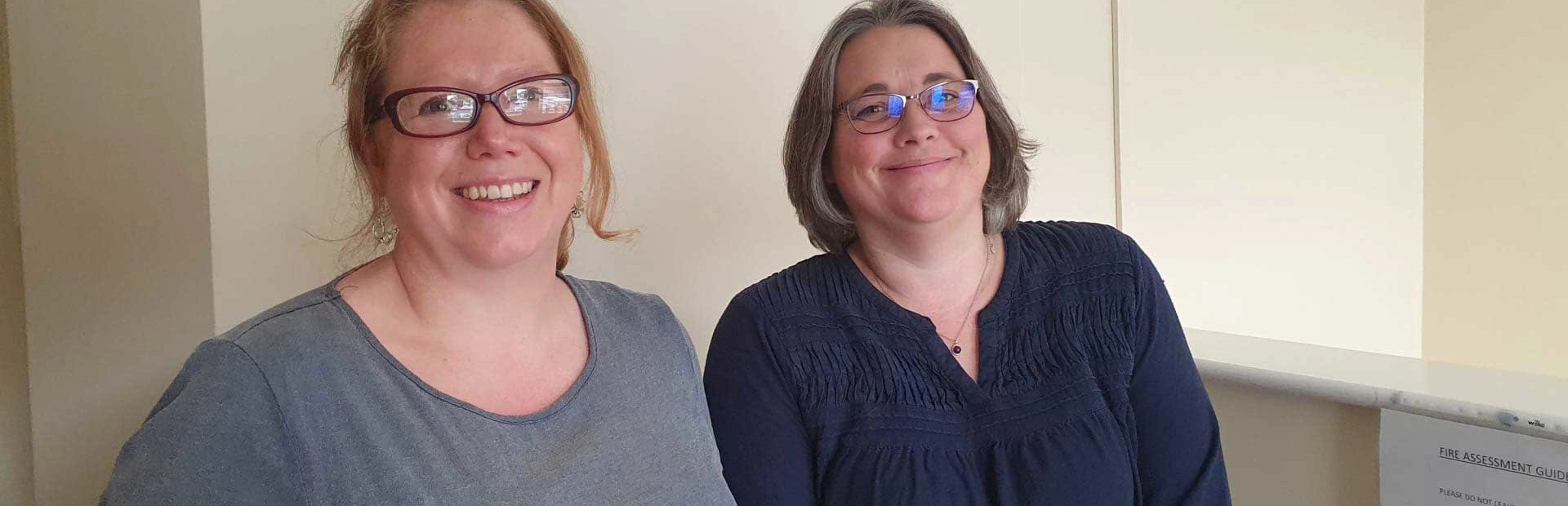 Close up of Sarah and Amy both wearing blue tops and smiling in an office Close up of Sarah and Amy both wearing blue tops and smiling in an office