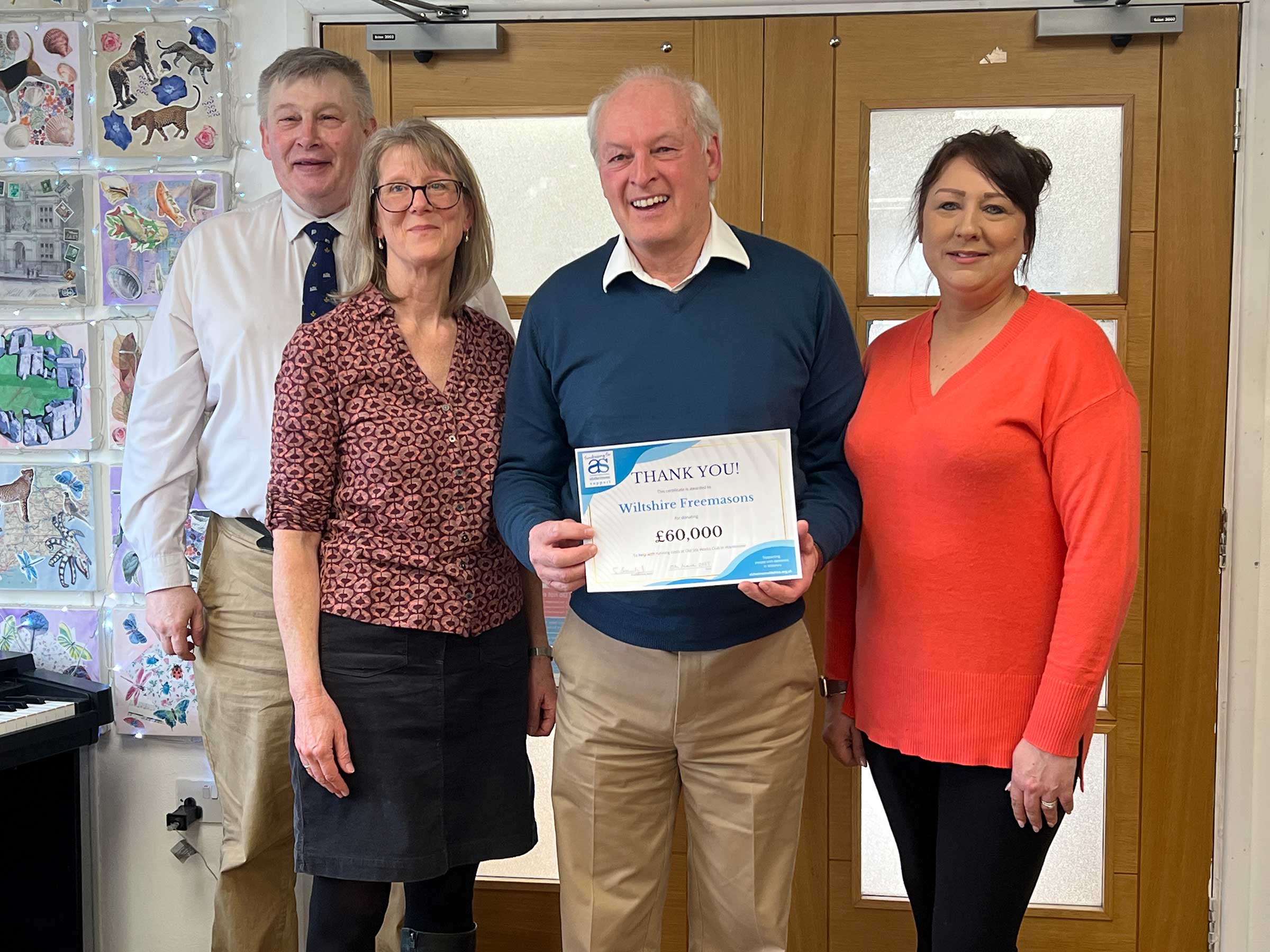 A small group of charity staff and representative of Wiltshire freemasons with their thank you certificate, standing in front of the entrance doors at Old Silk Works club