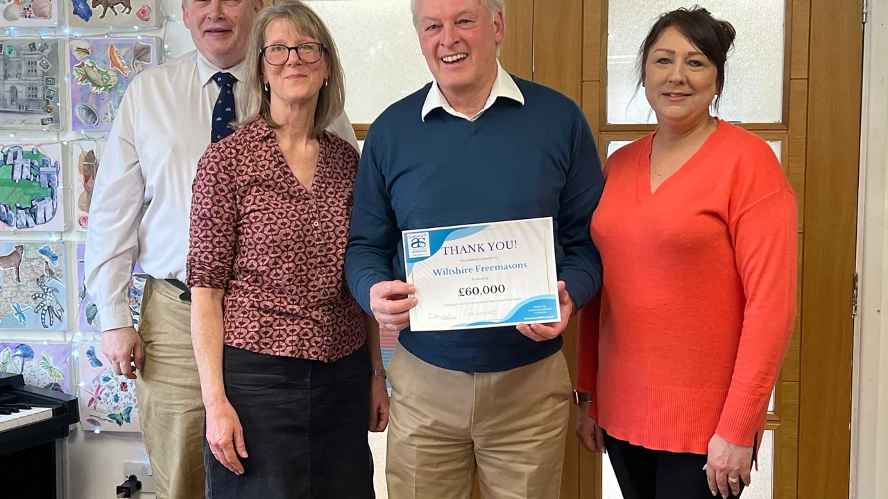 A small group of charity staff and representative of Wiltshire freemasons with their thank you certificate, standing in front of the entrance doors at Old Silk Works club