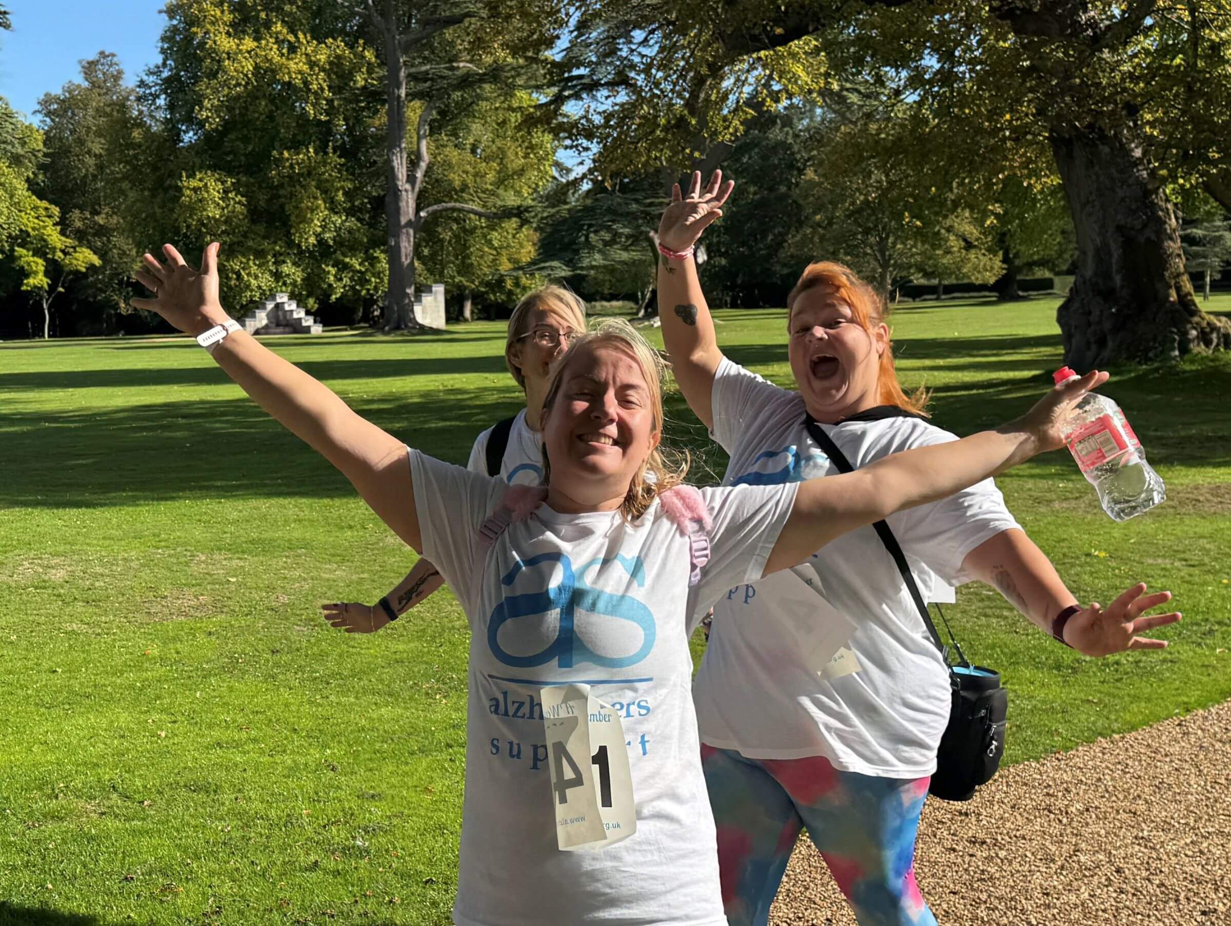 Three ladies in Alzheimer's Support t-shirts posing with their arms in their air at a sponsored walk