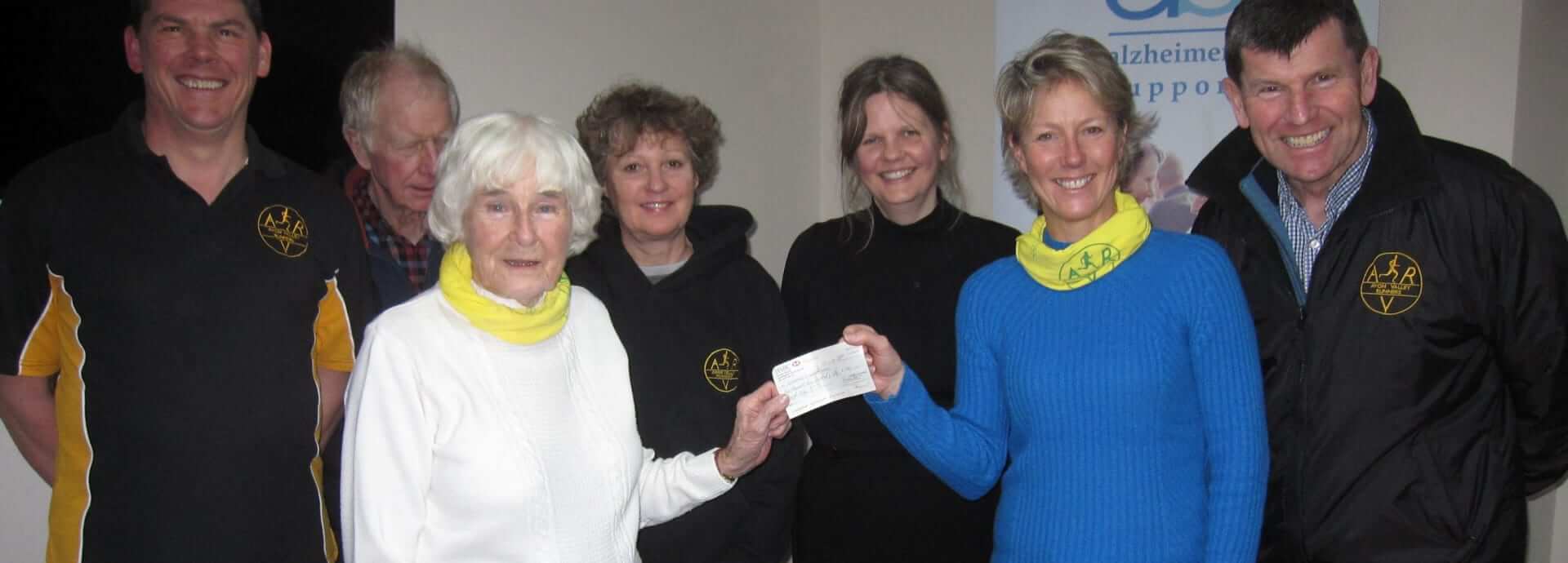 A group of seven people from Avon Valley Runners holding a cheque donation from Sheila the organiser 