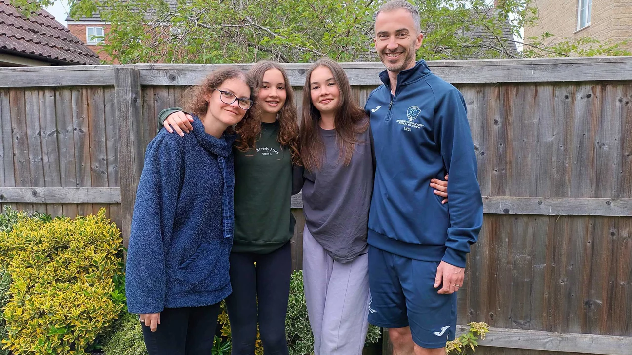 Claire and her family standing in a group with their arms around each other, in a garden setting in front of a wooden fence